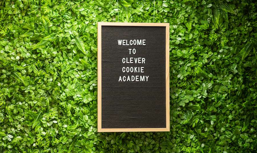 Sign saying "Welcome to Clever Cookie Academy" against a green decal wall.